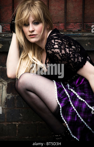 A young blonde woman wearing a purple skirt in a grungy location. Stock Photo