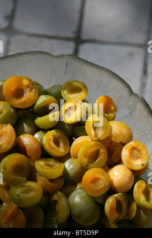 (Prunus x domestica var. syriaca) Halved and stoned Mirabelle plums in a glass bowl. Stock Photo