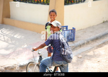 2 young boys playing in the street in the Dominican Republic. One boy is playing on a bike Stock Photo