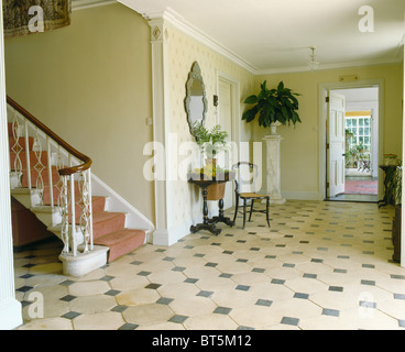 Cream+black stone tiled floor in large traditional cream hall with large houseplant on marble column Stock Photo