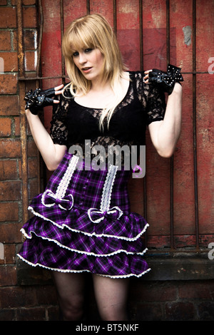 A young blonde woman wearing a purple skirt in a grungy location. Stock Photo
