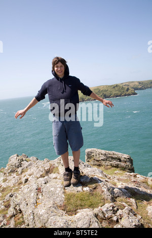 Teenage boy stands in strong wind on rocky headland above sea Stock Photo