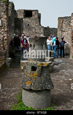 Tourists examine the excavated site of the Pistrinium (Bakery) with two flour mills in the foreground, Pompeii, Italy Stock Photo