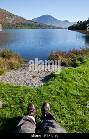 A Walker's legs and boots on the banks of Loweswater with Whiteside in the distance, (open access land) Lake District, Cumbria Stock Photo