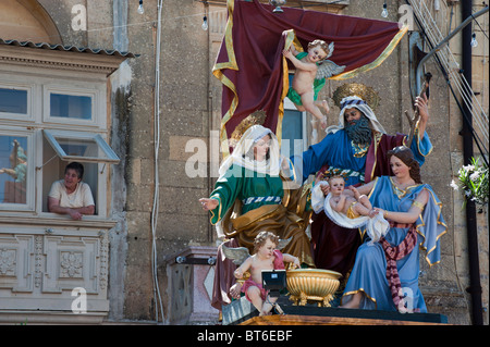 A picture of a women looking out of her window onto the main square.  The statues are ready for the forthcoming festa. Stock Photo