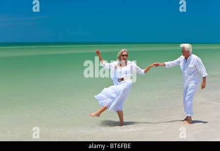 Happy senior man and woman couple dancing and holding hands on a deserted tropical beach with bright clear blue sky Stock Photo