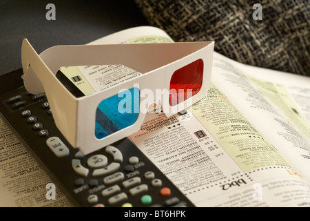 pair of 3d glasses and tv remote control sitting on top of televisions listings magazine on the arm of a chair Stock Photo