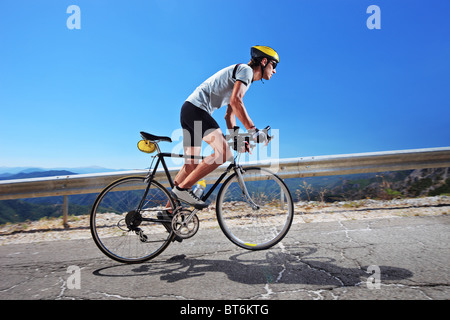 A male cyclist riding a bike uphill along a road Stock Photo