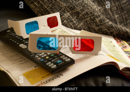 two pairs of 3d glasses and tv remote control sitting on top of televisions listings magazine on the arm of a chair Stock Photo