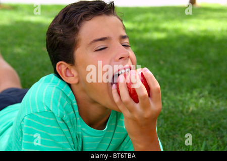 boy teenager eating red apple laying on garden grass outdoors Stock Photo
