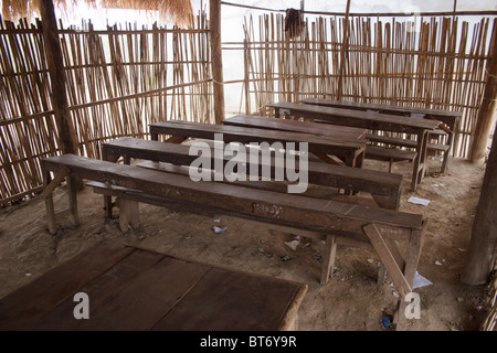 Old wooden tables in poor condition serve students and teachers in a room with a dirt floor at a primary school in communist Lao Stock Photo