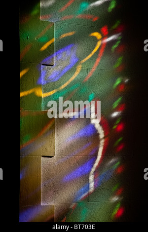 Coloured light patterns on the stone wall from a stained glass window inside St Peter's Church, Sawrey, Lake District, Cumbria Stock Photo