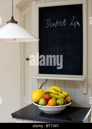 Close-up of pendant light beside blackboard on kitchen wall above dish of fruit on kitchen worktop Stock Photo