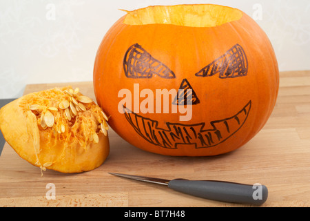 pumpkin partially turned into halloween jack-o-lantern with top cut out and facial features marked in pen with knife Stock Photo