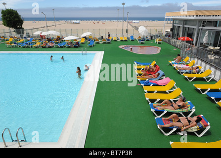 Group of people sunbathing by an outdoor swimming pool in front of the Figueira da Foz beach, Portugal Stock Photo