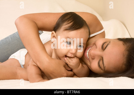 Mom and son lying down on bed and mother embracing the infant baby, who put his hand into mouth Stock Photo