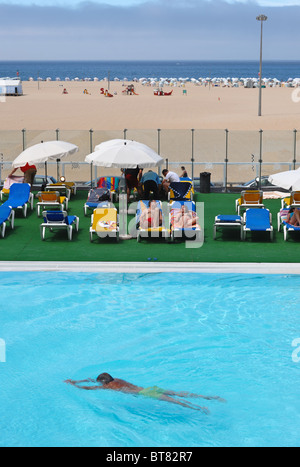 Man swims by a group of people sunbathing next to an outdoor swimming pool in front of the Figueira da Foz beach Stock Photo