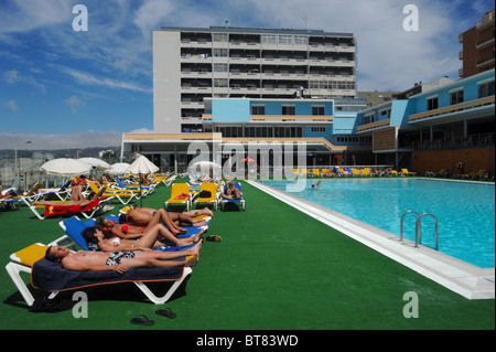 Group of people on lounge chairs sunbathing by a outdoor swimming pool Stock Photo