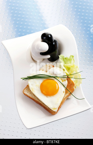 Toast with heart-shaped fried egg with chives and figures as salt and pepper shakers Stock Photo