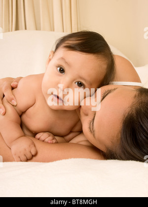 Mom and son lying down on bed and mother embracing the infant baby, who looks at camera with serious facial expression Stock Photo
