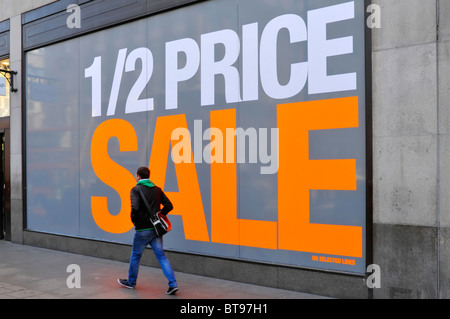 Large big shop window poster display promoting half price sale (store name digitally removed) dwarfing pedestrian on pavement London England UK Stock Photo