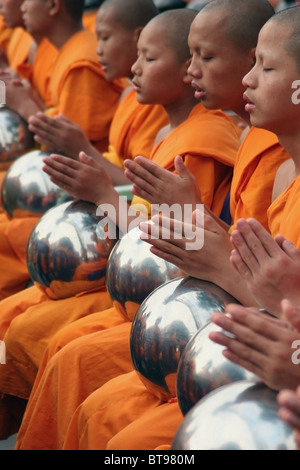 Buddhist monks wearing orange robes are praying with their alms bowls near Tha Pae Gate in Chiang Mai, Thailand. Stock Photo