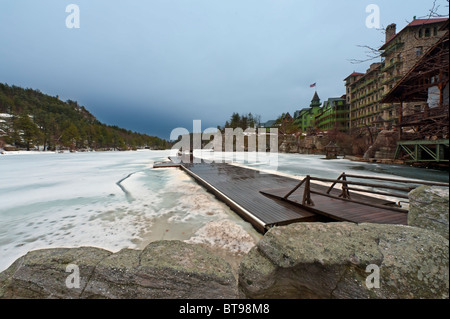 Lake Mohonk seen beyond rocks at shore, with view of long dock, mountains, Mohonk Mountain House, New Paltz, NY, USA. Stock Photo
