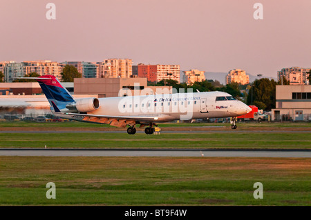 A Delta Connection (SkyWest Airlines) CRJ-200ER regional jet airliner lands at Vancouver International Airport (YVR) at sunset. Stock Photo