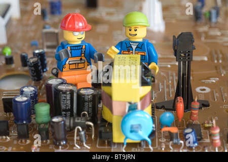 Lego engineers discussing their work on an electronic circuit board next to components including capacitors and resistors. Stock Photo