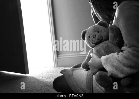 Young girl sitting holding a teddy bear, back view. Stock Photo