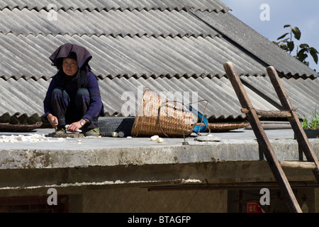 a minority woman sits on her roof while cutting prouce Stock Photo