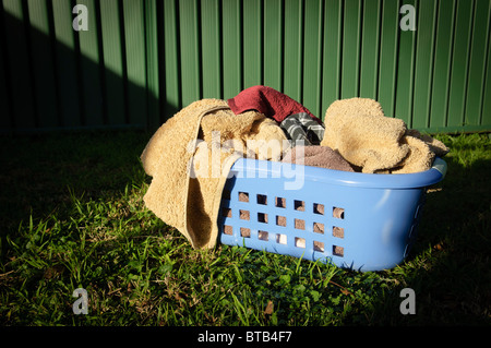 Blue laundry basket filled with towels sits on a lawn outside Stock Photo