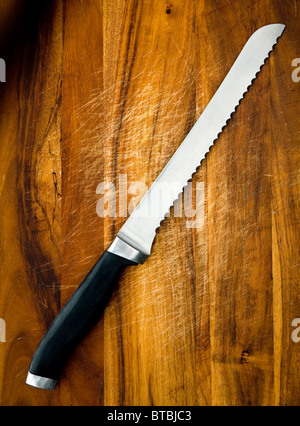 Large stainless steel bread knife on a wooden chopping board Stock Photo