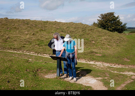 A retired couple looking at an information board at the Iron Age hill fort of Maiden Castle, Dorchester, Dorset. DAVID MANSELL Stock Photo