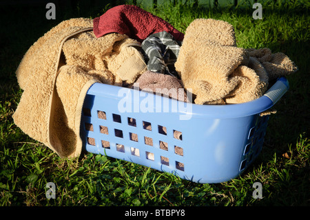 Blue laundry basket filled with towels sits on a lawn outside Stock Photo