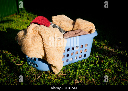 Blue laundry basket filled with towels sits on a lawn outside Stock Photo