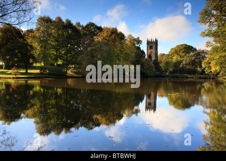 View of St James Church in Gawsworth across a lake showing the blue sky with clouds reflected in the lake. Stock Photo