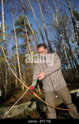 Man shooting with bow and arrow in forest, Stockholms Lan, Sweden Stock Photo