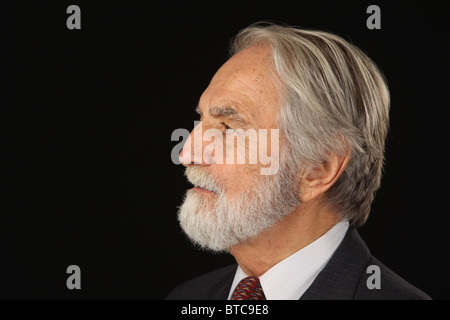 Profile portrait of bearded and grey haired senior businessman in suit and tie, studio shot, black background, October 16, 2010 Stock Photo
