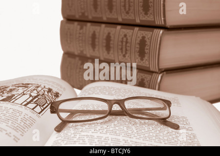 Glasses over opened old book with blurred old books in the background, in sepia Stock Photo