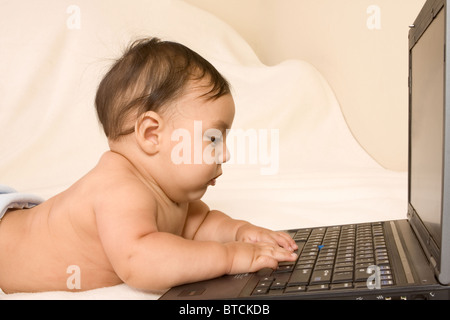 Infant Asian boy playing with laptop keyboard (profile view) Stock Photo