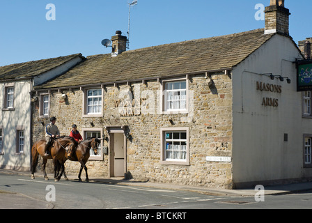 Two horse riders passing the Masons Arms pub in the village of Gargrave, North Yorkshire, England UK Stock Photo