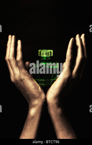 Men's hands in golden paint holding green bottle of perfume on black backgroun Stock Photo