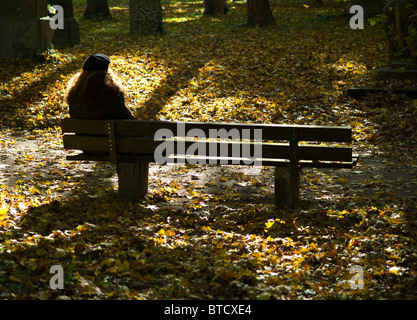 Single woman wearing a beret sitting on a bench in a graveyard - autumn / fall in Munich, Germany Stock Photo