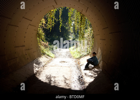 A disused railway tunnel has been converted to a footpath and a young boy sits in it Stock Photo
