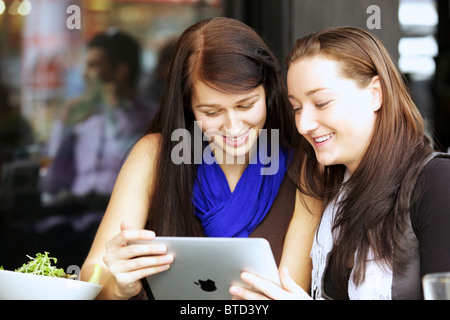 Close up of two beautiful young woman reading from an iPad at a restaurant or cafe Stock Photo