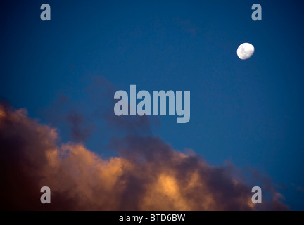 Almost full bright white moon rises over last light in the clouds Stock Photo