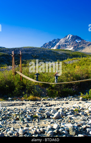 Hikers cross a suspension bridge over College Creek on their way to Gulkana Glacier, Southcentral Alaska Stock Photo