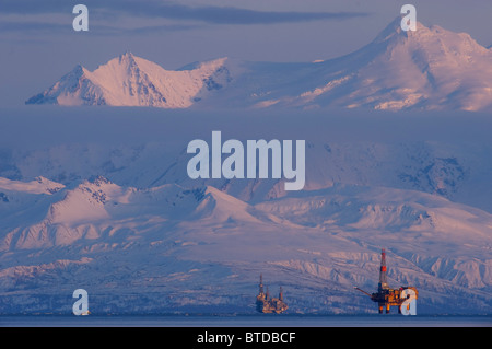 Three drill rigs in Cook Inlet with Mt. Spurr looming large in the background at sunset, Southcentral Alaska, Winter Stock Photo