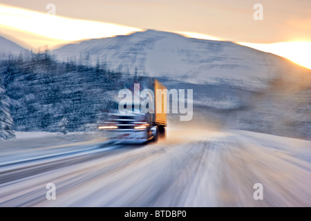 Semi truck driving on the snowcovered Seward Highway at sunrise, Southcentral Alaska, Winter Stock Photo